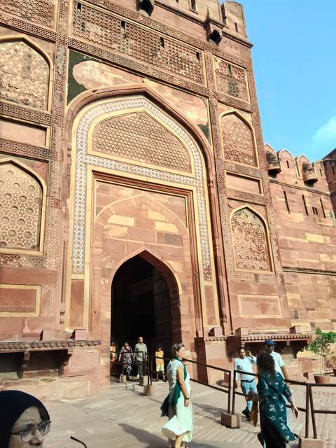       Tall ornate gateway of red sandstone with intricate inlay work in Agra Fort under blue skies.
  