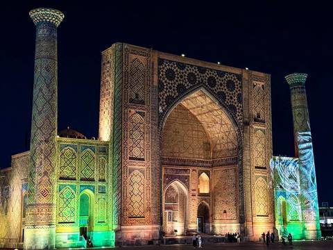       Illuminated Islamic madrasah with ornate tilework glowing against the dark night sky.
  