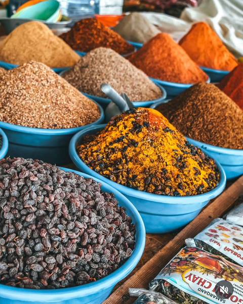       Mound of vibrant yellow and red spices in a blue bowl at an Uzbek market.
  