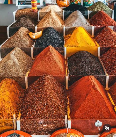       Array of neatly stacked spice pyramids in assorted colors at a bazaar stall.
  