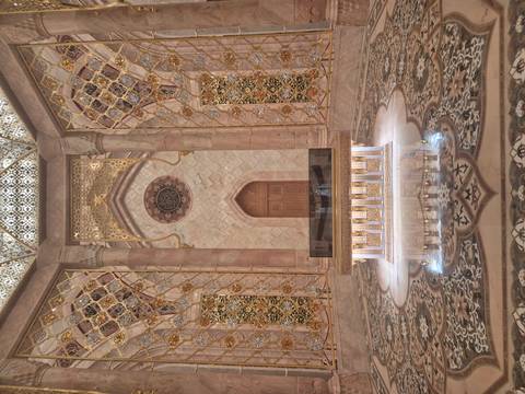       Opulent interior chamber with intricate golden mosaics, marble floor and central sarcophagus.
  