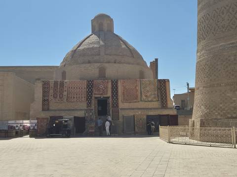       Brick domed building draped with colorful carpets at the entrance to a traditional craft shop.
  
