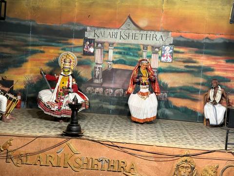       Traditional Kathakali dance performance on an indoor stage with colorful backdrops and musicians.
  