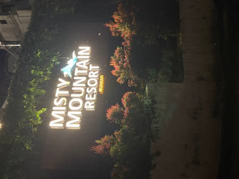       Illuminated sign for Misty Mountain Resort surrounded by foliage at night.
  