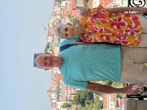       Smiling couple with cityscape of Lisbon’s colourful hillside buildings in the background on a sunny day.
  
