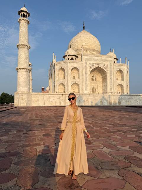       Woman in sunglasses standing on the marble platform of the Taj Mahal at sunrise light.
  