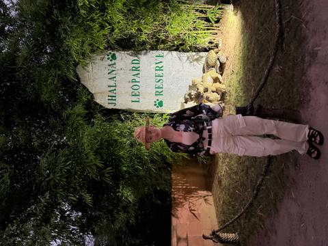       Woman standing by a stone sign for Jhalana Leopard Reserve surrounded by lush foliage at dusk.
  