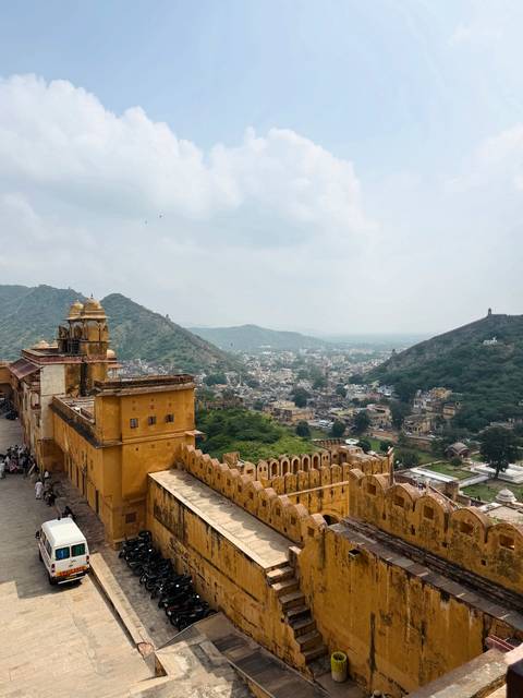       Panoramic view from a yellow-walled hilltop fort overlooking the city and surrounding green hills.
  