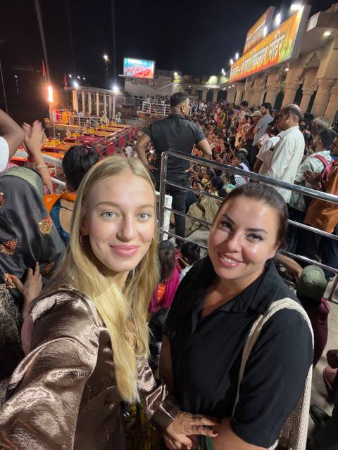       Two women take a close-up selfie amid a crowded evening ceremony with vibrant colours.
  