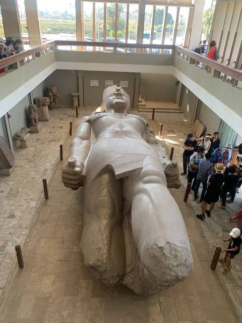       Giant fallen statue of Ramses II fills a museum hall while visitors observe from the sides.
  