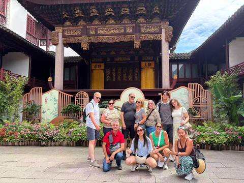       Tourists gather in a traditional Chinese garden courtyard before an ornate wooden stage.
  