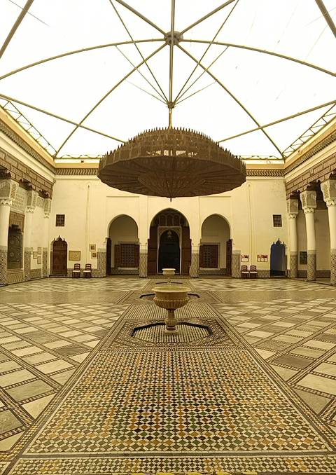       Elegant Moroccan courtyard with mosaic floors, arched doorways and a central fountain beneath a grand chandelier.
  