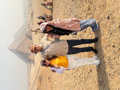       Three tourists pose with camels in front of the hazy pyramids on the Giza Plateau.
  