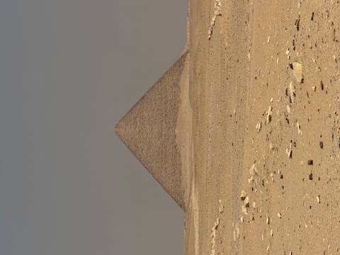       Isolated pyramid rises from the flat, sandy expanse under a muted desert sky.
  
