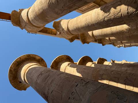       Towering carved sandstone columns of Karnak Temple reach up toward a deep blue sky.
  