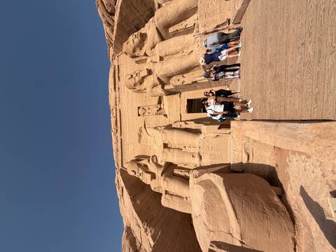       Tourists gather at the colossal seated statues and entrance of Abu Simbel carved into sandstone cliffs.
  