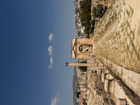       Stone archway and column line the ancient cardo of Jerash with the modern town visible beyond.
  