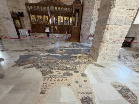       Ancient mosaic map of the Holy Land covers the church floor in Madaba behind rope barriers.
  