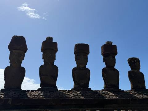      Silhouetted moai with pukao topknots stand in sharp contrast against a bright sky.
  