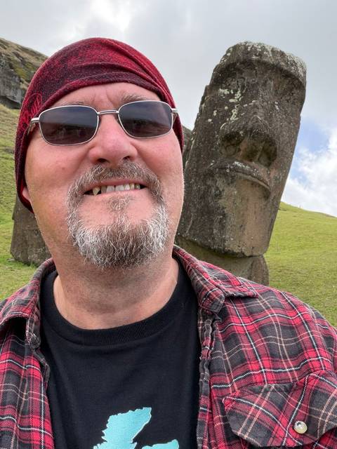       Close-cropped selfie of a man with a moai statue looming behind on grassy hillside.
  
