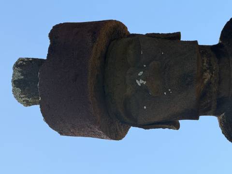      Close-up vertical view of a single moai statue with topknot under clear blue sky.
  