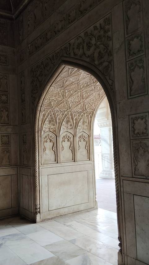       Intricately carved marble archway with floral motifs inside a Mughal monument.
  