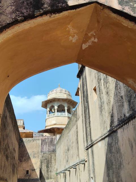       Stone archway frames a small domed watchtower against a bright blue sky.
  