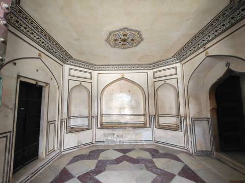       A small octagonal room with faded frescoes, arched niches, and patterned floor tiles.
  