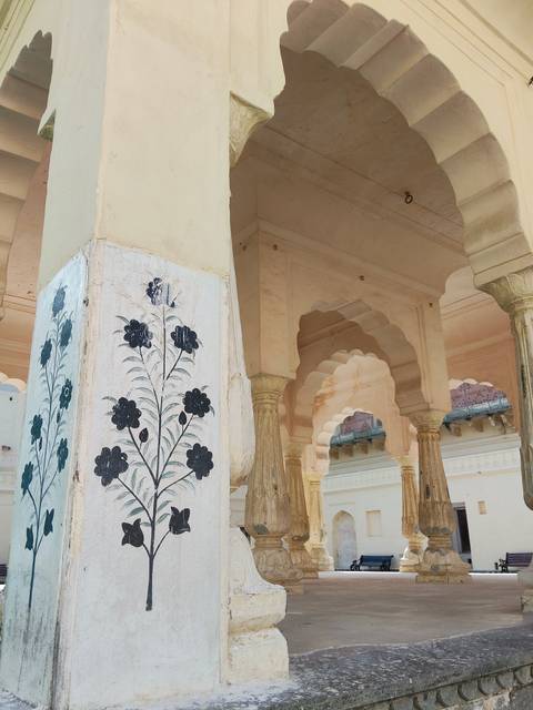       Marble pillar painted with black floral motifs amid scalloped sandstone arches.
  