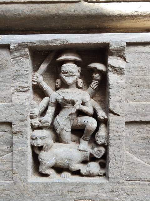       Ancient stone carving of a multi-armed deity set into a weathered wall.
  