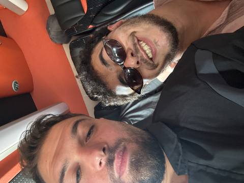       Two young men smiling for a close selfie inside a vehicle.
  