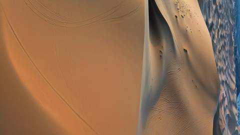       Expansive view of smooth orange sand dunes with vehicle track patterns.
  