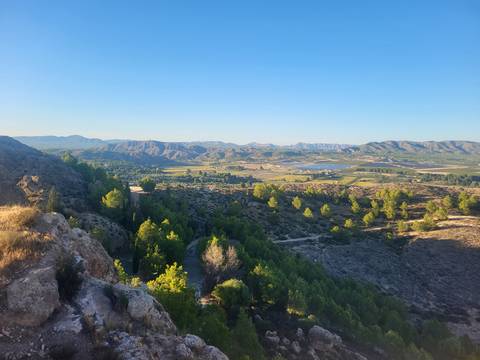       Wide valley landscape of Murcia with patchwork fields, reservoirs and surrounding mountain ranges under a clear sky.
  