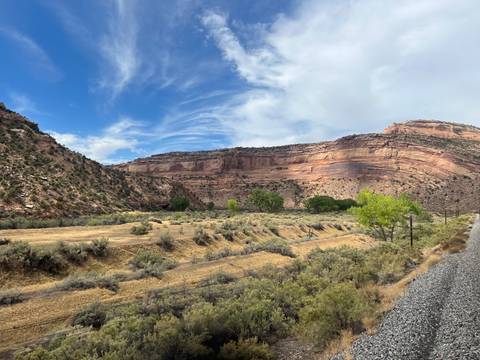       Railway line running through arid canyon with layered sandstone cliffs and blue sky
  