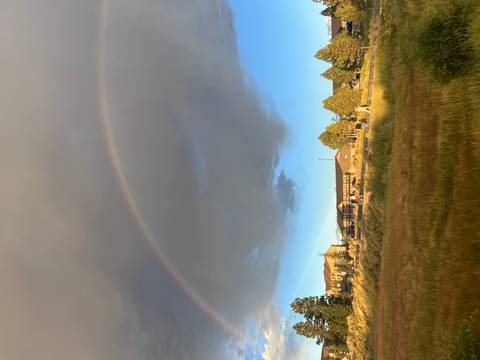       Rainbow arching over lodge buildings and grassy meadow under dramatic clouds
  