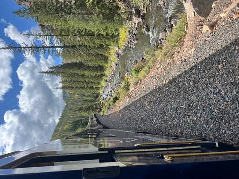       Scenic train traveling beside rocky river through evergreen forest
  