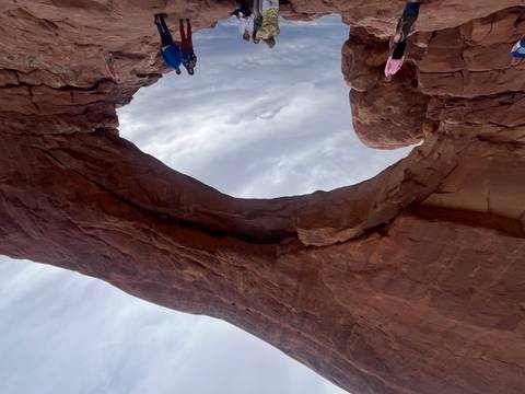       Massive natural sandstone arch spanning cloudy sky with visitors below for scale
  
