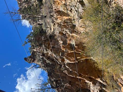       Steep reddish rock cliff with sparse shrubs and several power lines crossing the scene beneath a deep blue sky.
  