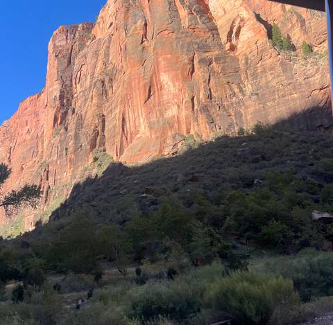       Massive orange canyon wall partly in shadow with vegetation at its base under a clear blue sky.
  