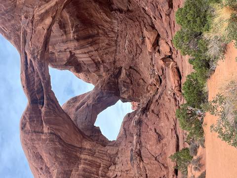       Dramatic twin sandstone arches tower above hikers exploring the rocky terrain below.
  