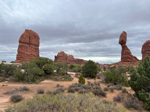       Wide desert vista featuring balanced red rock columns and scattered shrubs beneath a moody sky.
  