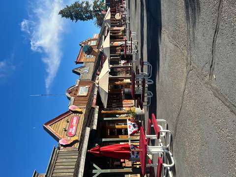       Colorful Old West-style storefronts with red picnic tables lining a sunny boardwalk street.
  