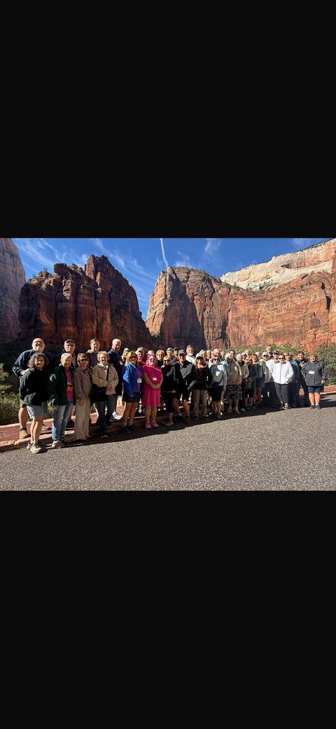       Large tour group posing on a canyon road framed by towering red rock walls.
  