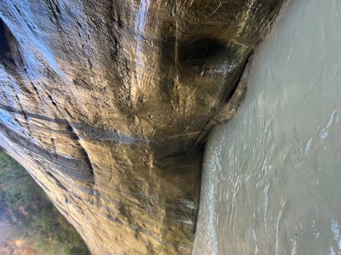       Close view of canyon wall meeting murky flowing water in a narrow gorge.
  