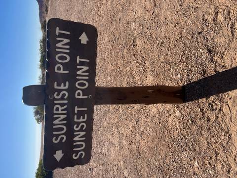       Directional wooden sign pointing to Sunrise and Sunset Points set against a bright desert sky.
  