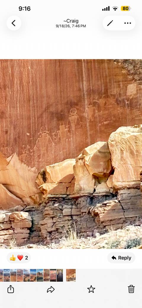       Faded petroglyphs etched into a red rock wall beside angular sandstone blocks.
  