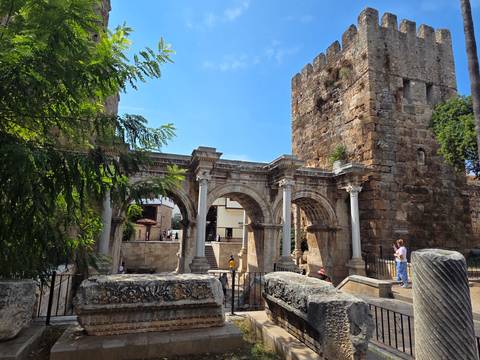       Roman-era stone arches and towers of Hadrian's Gate with tourists exploring the historic site.
  