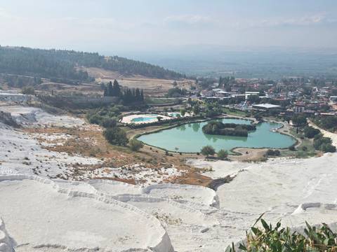       Panoramic view of green ponds and travertine terraces at Pamukkale with town in the background.
  