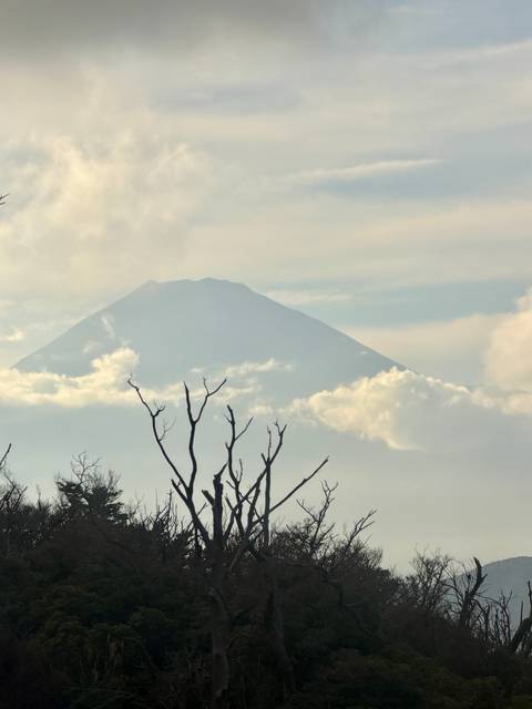       Mount Fuji’s silhouette rises above drifting clouds on a hazy day.
  