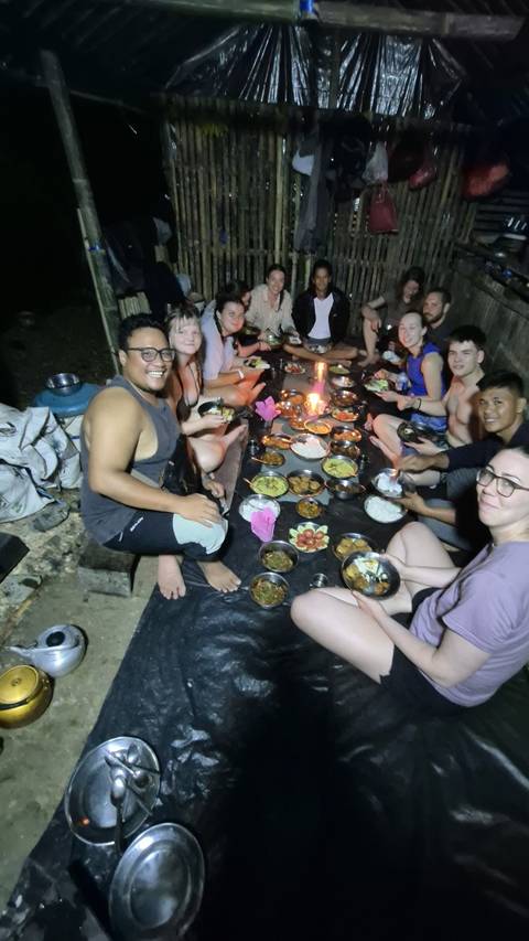       Travellers sit barefoot on ground tarps around a spread of local dishes and candles during a jungle camp dinner.
  